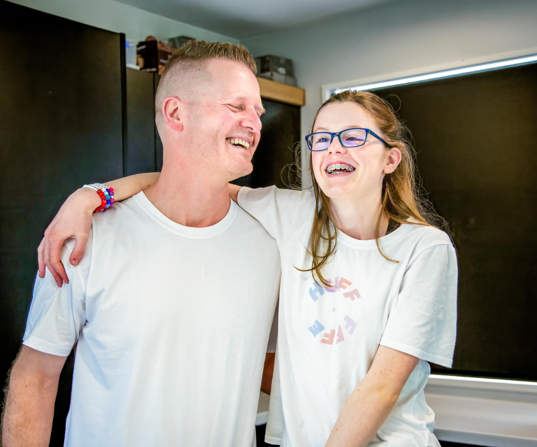 Asha and her Father stand in their kitchen, smiling.