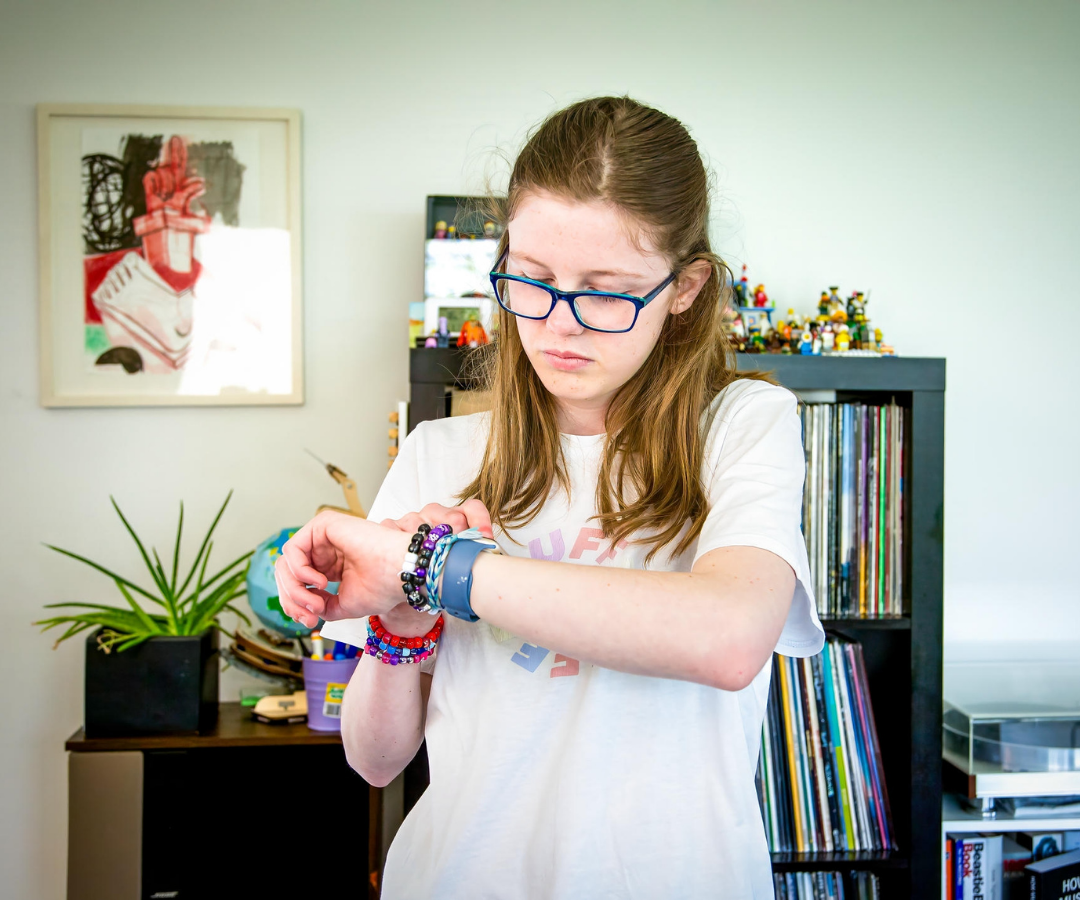 Asha, a 14 year old girl with low vision, stands looking at her watch in her home.