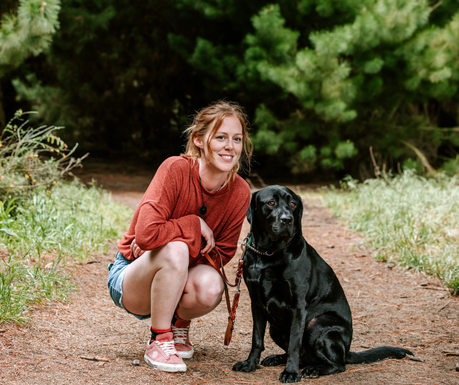 Laura, a young woman with red hair, kneeling next to her black guide dog Ryder, in a park. Laura, a young woman with red hair, kneeling next to her black guide dog Ryder, in a park.