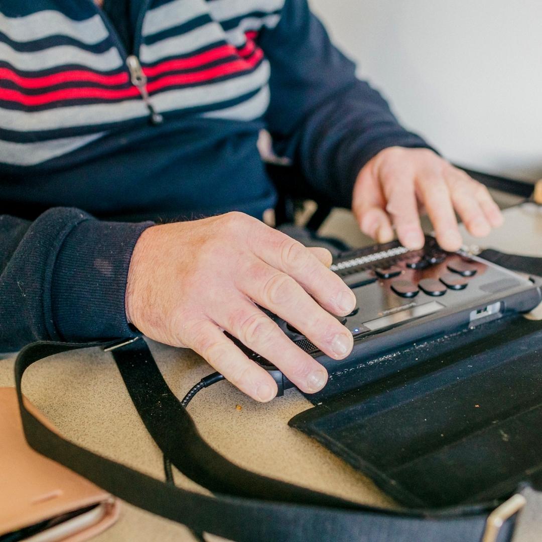 A close up of a man's hands using a Braille Machine A close up of a man's hands using a Braille Machine