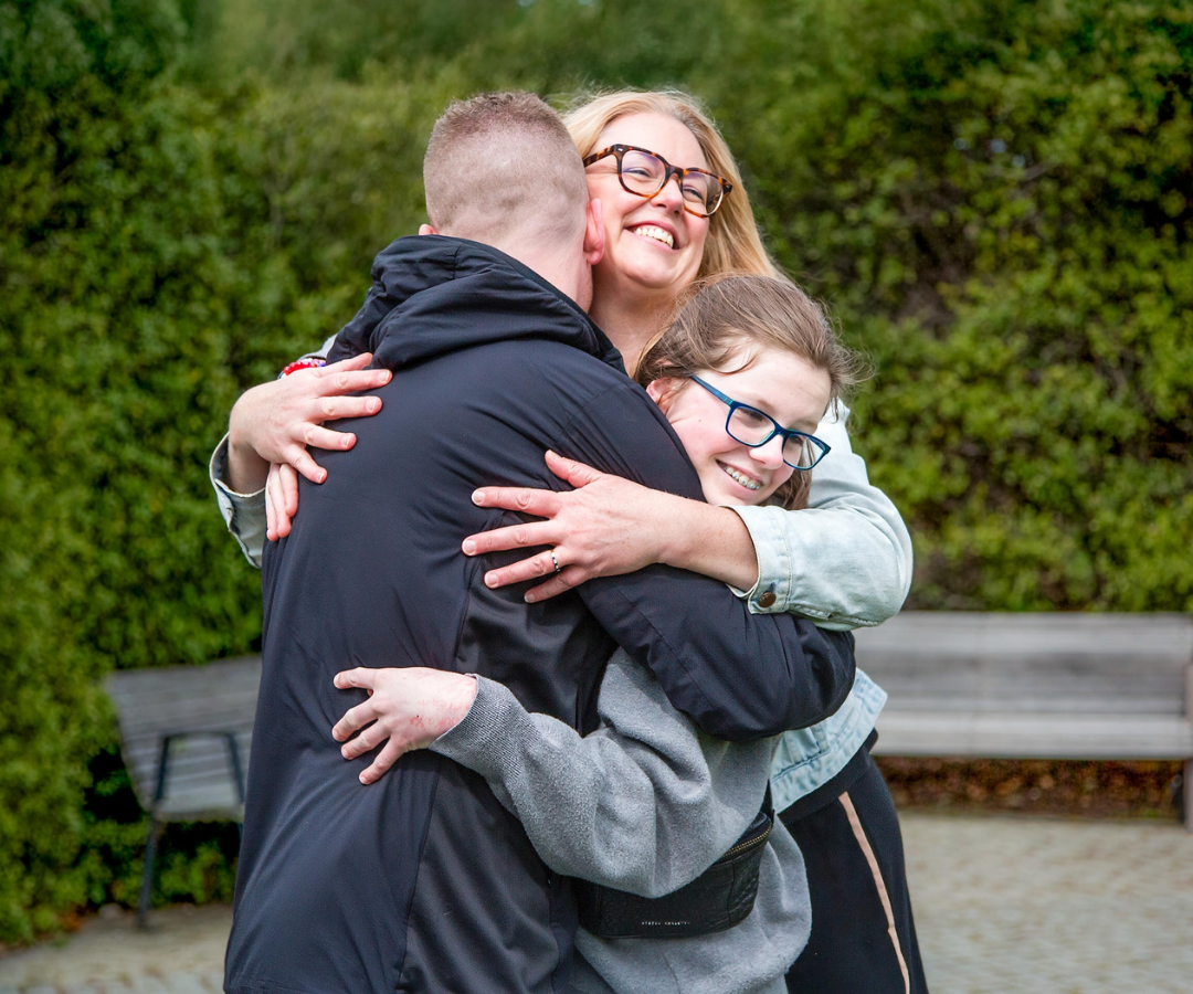 Asha, her mum and her brother sharing a hug in the park.